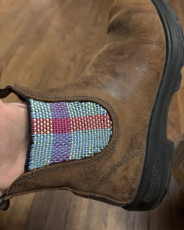 Brown leather Chelsea boot whose side gusset has been rewoven in a checked pattern of pink, blue and yellow yarn.