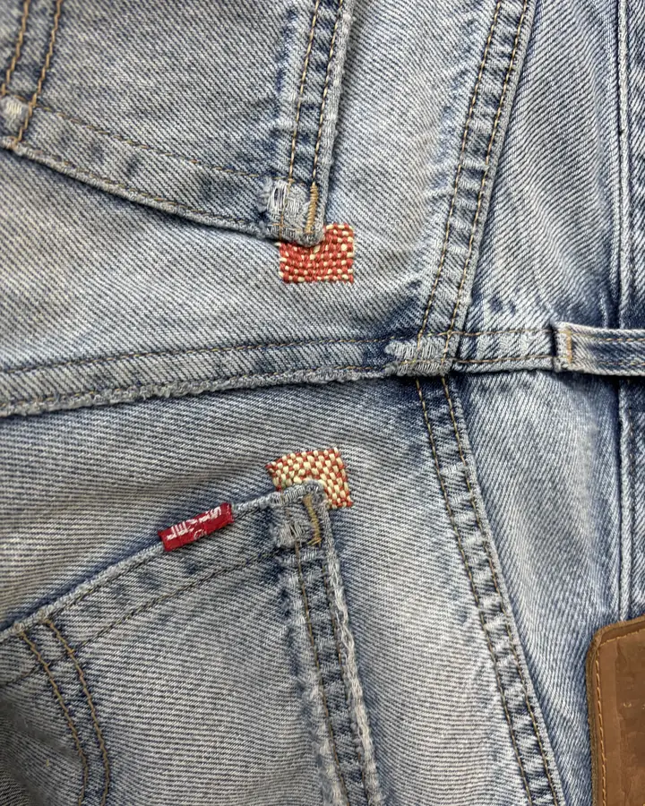 Light-wash Levi's with two small woven darns in orange and red at the corners of the pockets.