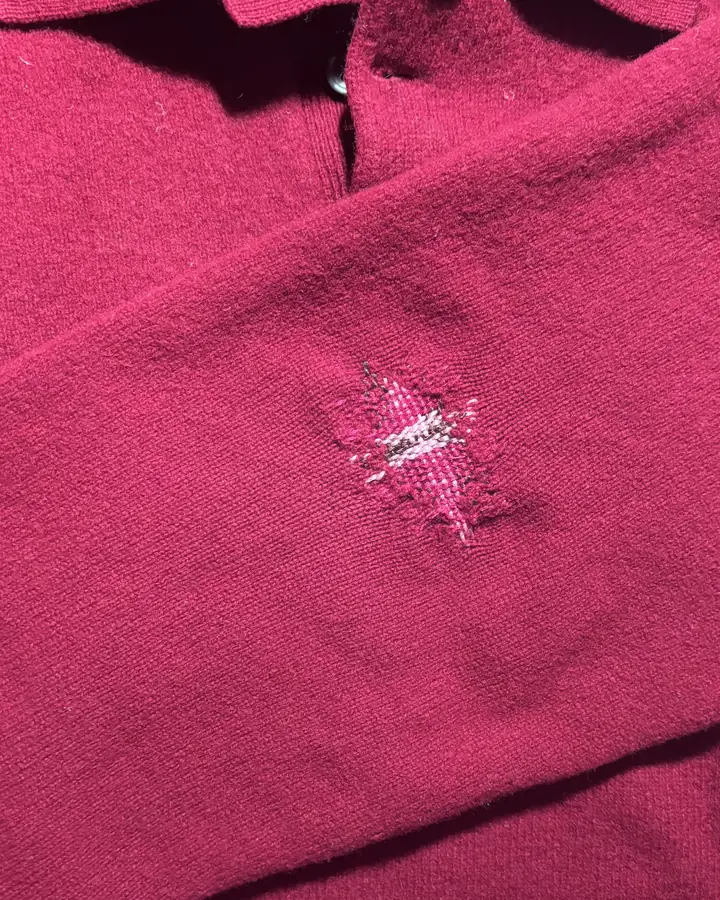 Deep red knitted sweater with a small woven darn closing a hole below the collar.