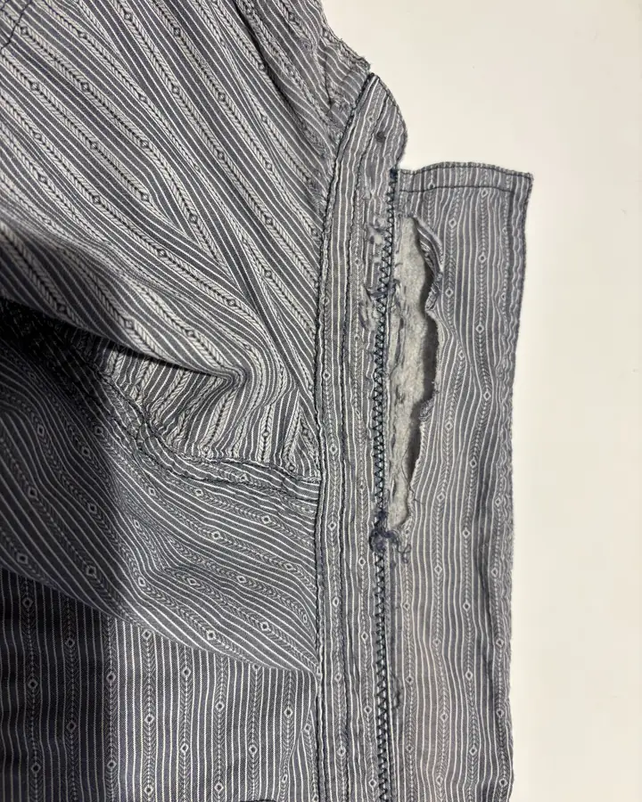 Striped cotton shirt with the placket edge worn through into a ragged strip of loose pale fibre.
