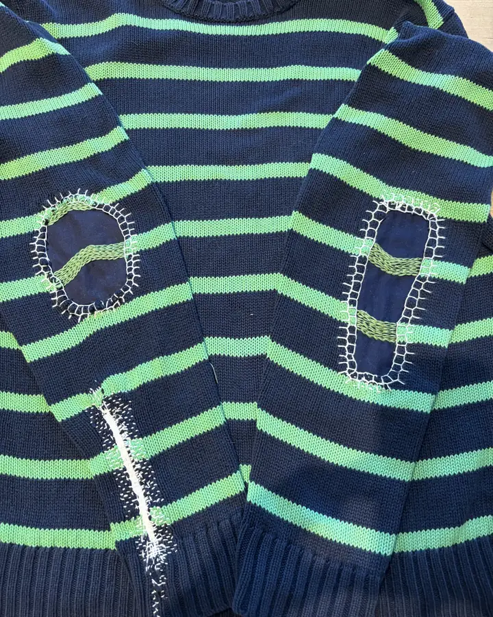 Navy and green striped sweater with an oval patch on each elbow, edged in pale blanket stitch.